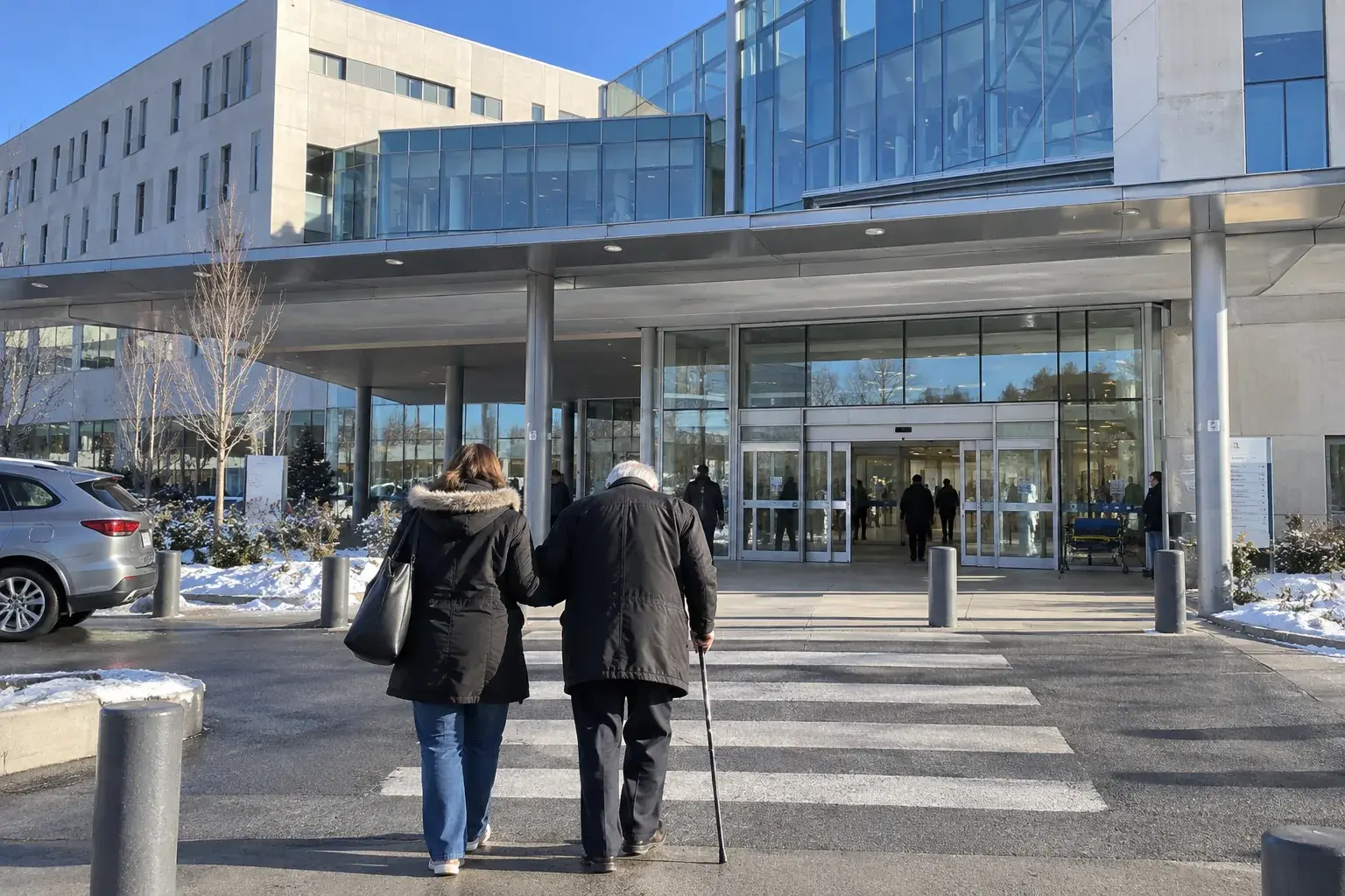 L’entrée d’un hôpital : un patient âgé avec une canne et une accompagnatrice vus de dos, avant un trajet en taxi conventionné ou en VSL